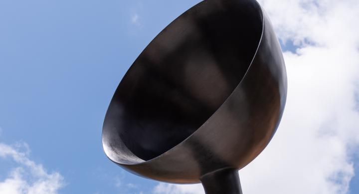 A bronze sculpture with a bowl shape set against a blue sky with clouds